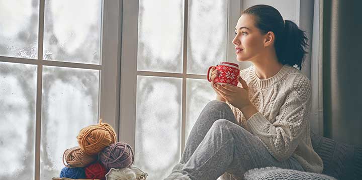 Woman sitting by window with a hot drink during winter